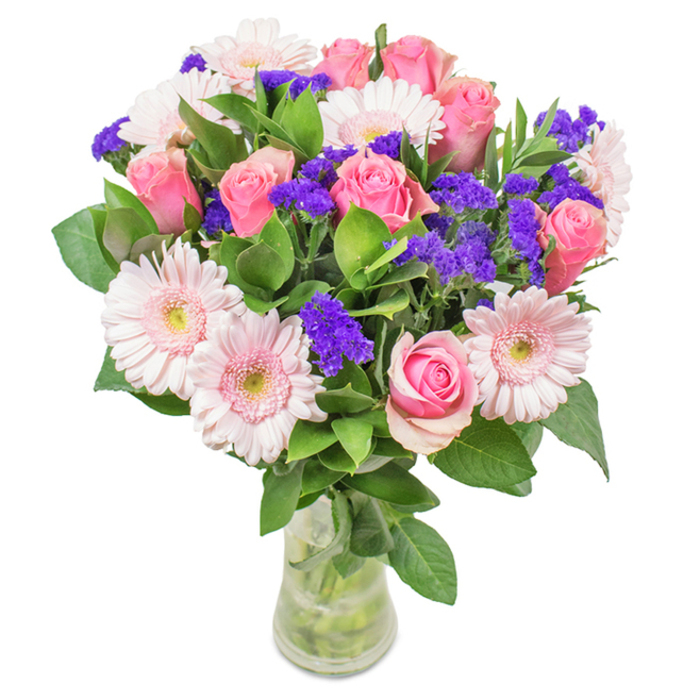 A graceful, locally-inspired bouquet sits poised in a clear glass vase, its composition thoughtfully arranged by a Lea Bridge florist attuned to the natural nuances of East London. The centrepiece features around eight velvety pink roses, their petals unfurling in exquisite spirals-some tightly wrapped, some just on the cusp of blooming, all evoking classic romance and gentle affection. Framing these roses are six to seven blush-toned gerbera daisies, each with large, rounded heads and radiating petals that fade into whisper-soft near-white centers, echoing the soft light of the mornings by Jubilee Pond. Threaded throughout this arrangement are lively clusters of bold purple statice, their textured accents magnifying the pinks and adding unexpected depth, much like wild patches of colour found along the Lea Bridge greenways. A lush layer of deep green foliage encircles and cradles each bloom, creating structure, contrast, and a flourish of fresh vitality-the sort of greenery you'd expect to find after a spring rain by Marshes Path. The transparent vase anchors the arrangement with calm clarity, revealing intertwining stems and crystal-clear water, suggesting both freshness and sincerity. Ideal for birthdays, anniversaries, or as an affectionate gift just because, this local bouquet, available for same-day delivery across Lea Bridge, delivers emotion as much as beauty-a true celebration of nature and heartfelt artistry rooted in our North East London neighbourhood.